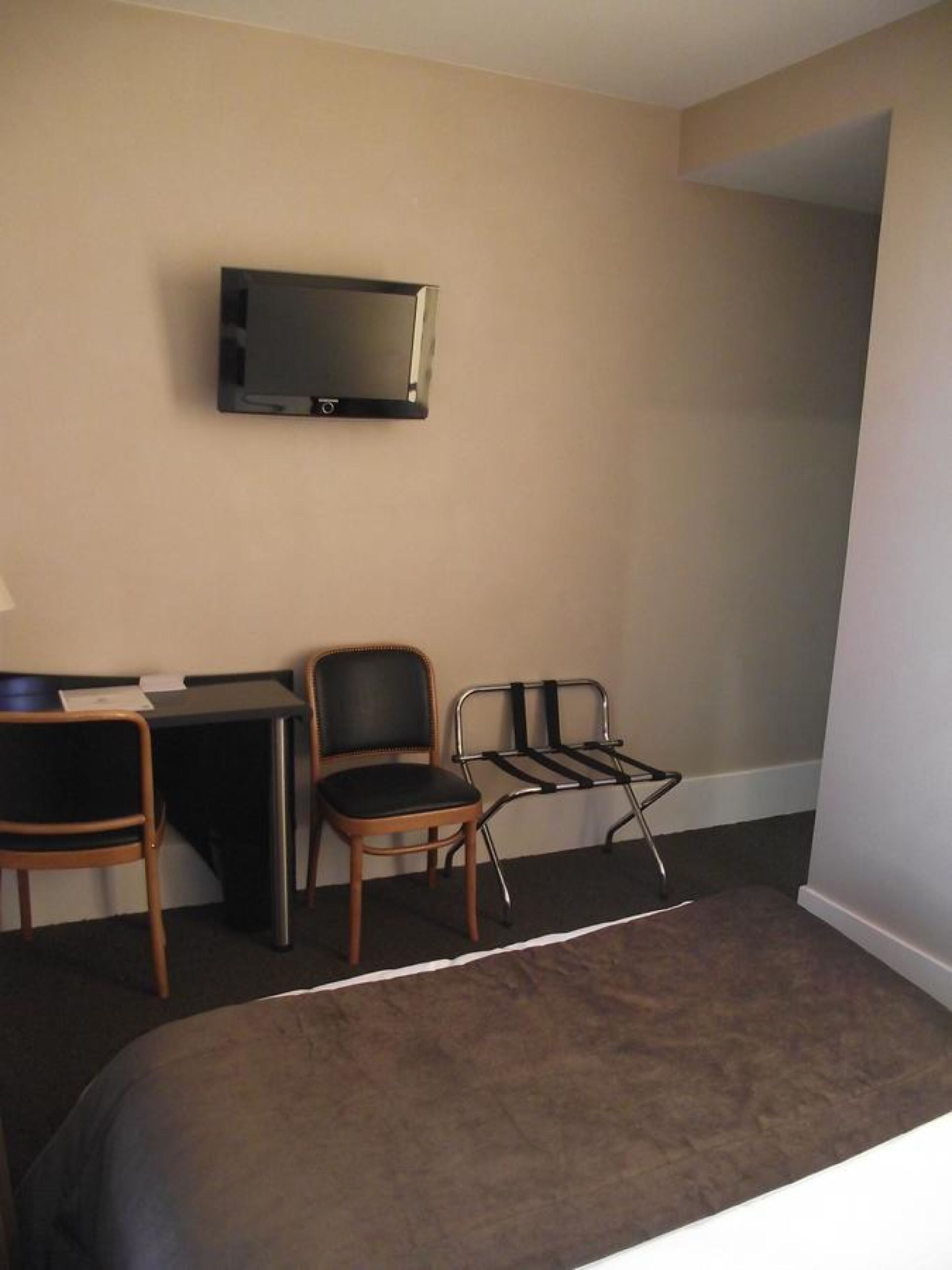 Habitación de hotel con una cama, un escritorio, una silla, un televisor montado en la pared y una mesita.