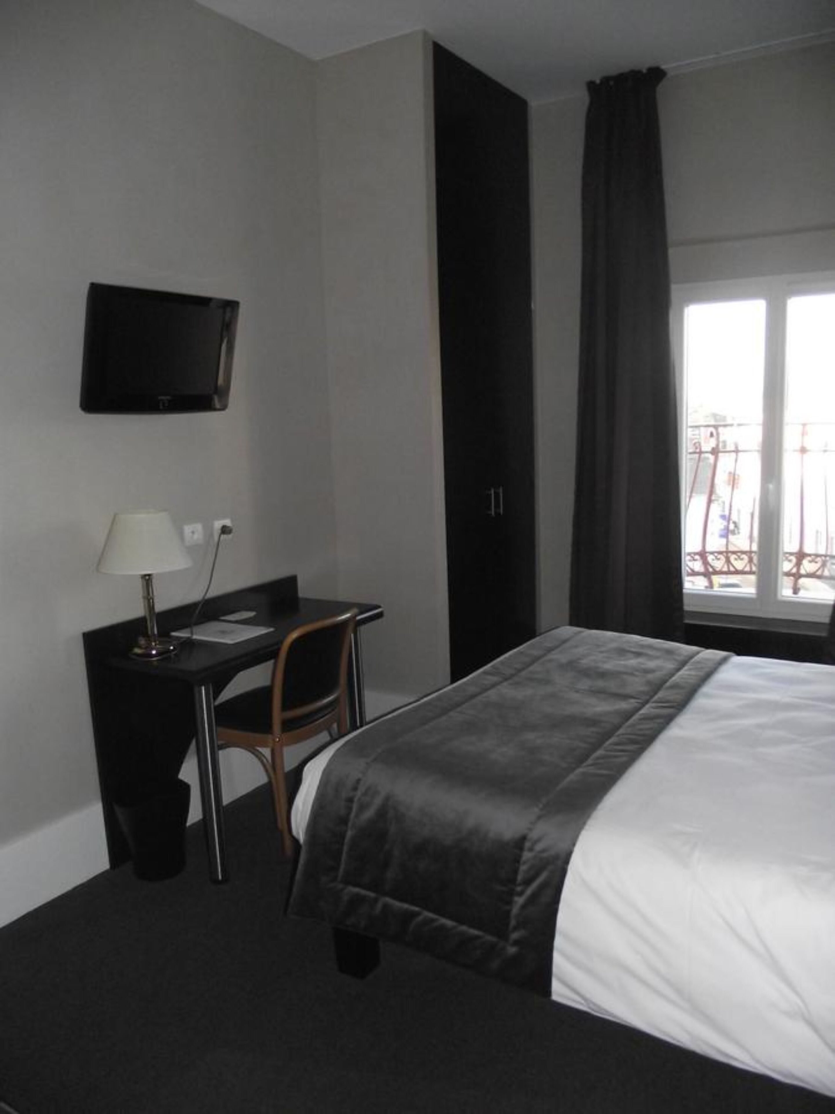 Habitación de hotel con cama, escritorio, silla, televisor montado en la pared y ventana con cortinas.