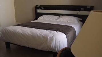 A hotel room with a bed, a chair, a desk, and a painting on the wall.