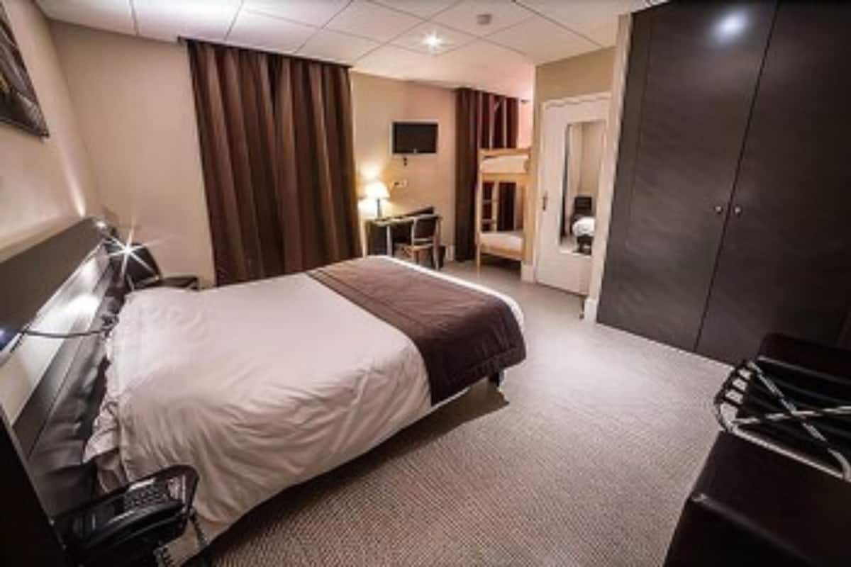 A hotel room with a bed, a desk, a chair, a wardrobe, and a television.