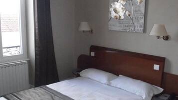 A hotel room with a bed, a window with curtains, two bedside lamps, and a wall-mounted artwork.
