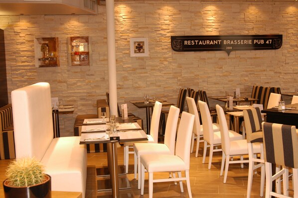 A restaurant interior with stone walls, white upholstered seating, and a sign reading "RESTAURANT BRASSERIE PUB 47".