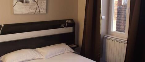 Una habitación de hotel con una cama grande, un cabecero, una ventana con cortinas y una obra de arte colgada en la pared.
