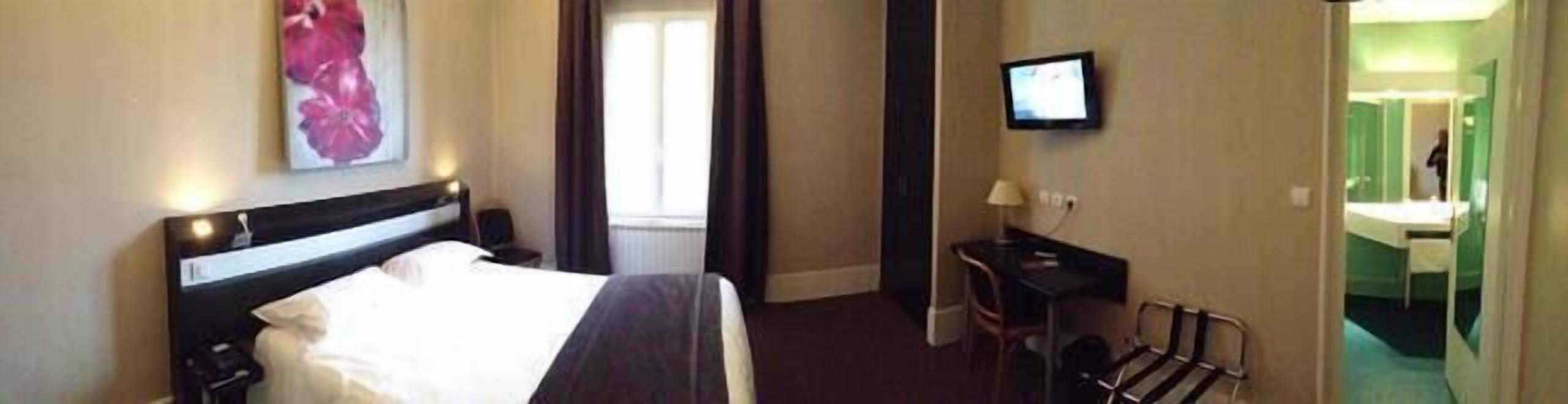 Habitación de hotel con cama, escritorio, televisión y baño visible a través de una puerta abierta.