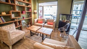 A cozy living room with a sofa, armchairs, a coffee table, and a bookshelf filled with books and decorative items. - Hôtel des Bourbons (Montlucon)