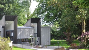 A modern building with a glass facade, surrounded by lush greenery and a well-maintained garden.