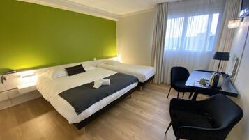 Habitación de hotel con dos camas, un escritorio con silla, una lámpara y una ventana con cortinas.