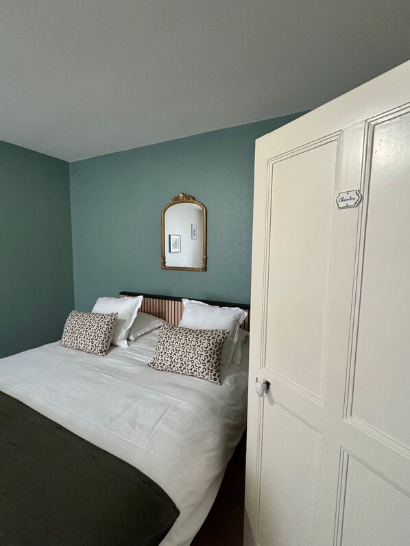 A bedroom with a bed, pillows, a mirror, and a door. - Citotel Le Clos Du Pontic (Landerneau)