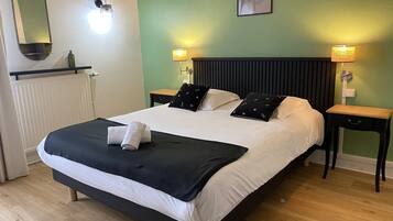 Una cama bien tendida con ropa de cama blanca y negra, dos mesitas de noche con lámparas, un espejo en la pared y un cuadro enmarcado.