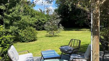 A deck with wicker chairs and a table, surrounded by greenery and a clear view of a distant building.