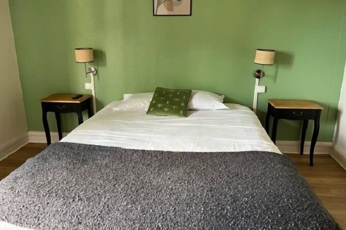 Quarto com uma cama, duas mesas de cabeceira, uma parede verde e um quadro emoldurado acima da cama.