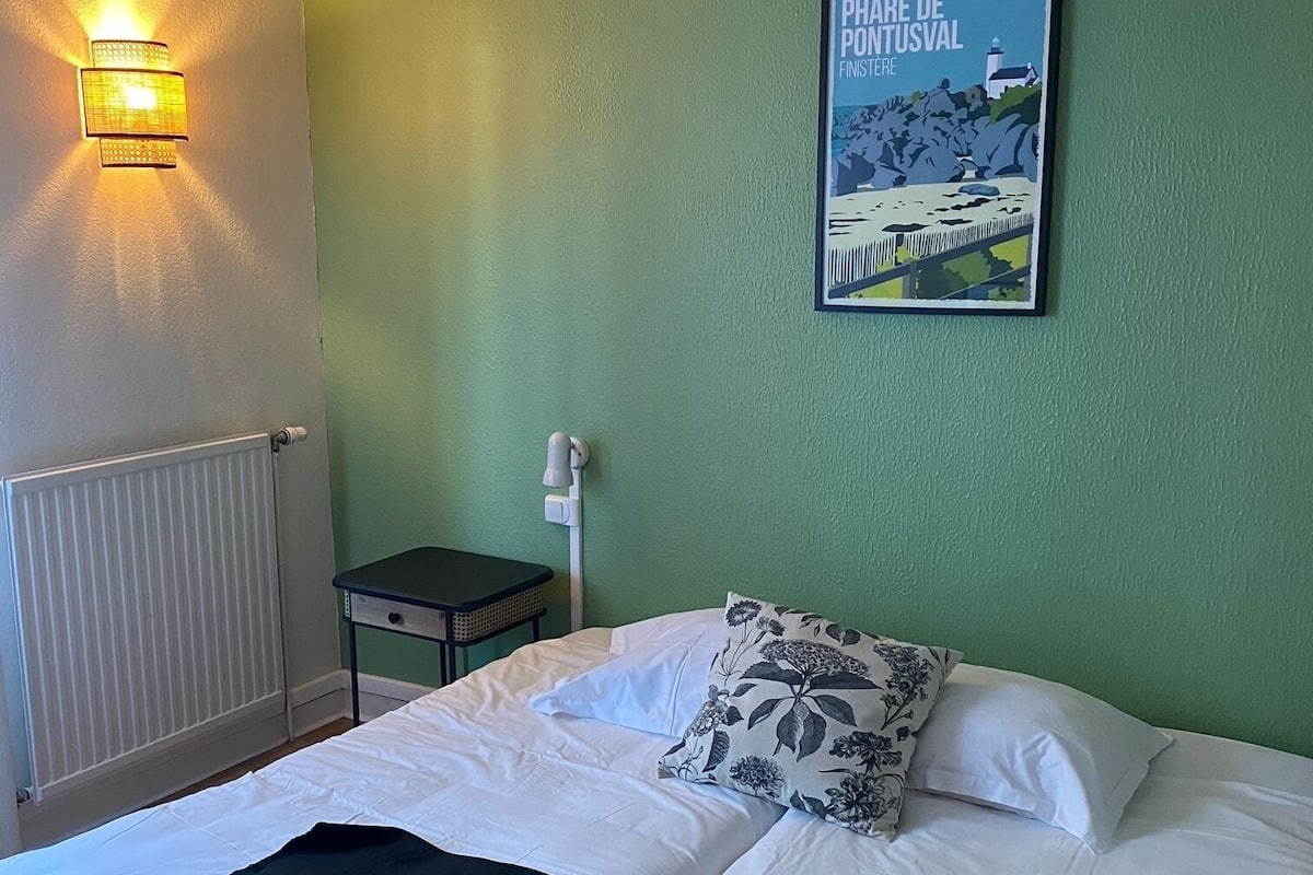 Quarto de hotel com uma cama, mesa de cabeceira, luminária, um quadro na parede e radiador.
