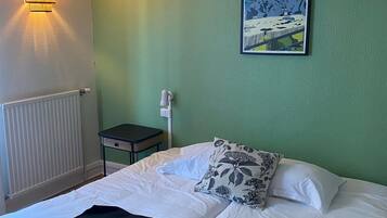 Una habitación de hotel con una cama, una mesita de noche, una lámpara, un cartel en la pared y un radiador.
