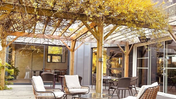 An outdoor patio area with wicker furniture, a pergola, and a view of the interior through glass doors.