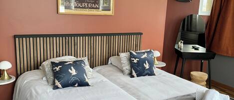 A double bed with two pillows, a bedside table with a lamp, a mirror, and a poster on the wall.