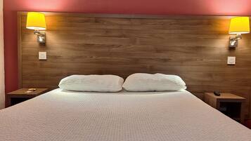 A neatly made bed with a textured white cover, two pillows, and two bedside lamps with yellow shades.
