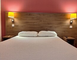 A neatly made bed with a textured white cover, two pillows, and two bedside lamps with yellow shades.