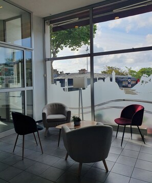 Un interior moderno con ventanas amplias, un sillón color beige, una silla roja y una pequeña mesa con una planta.