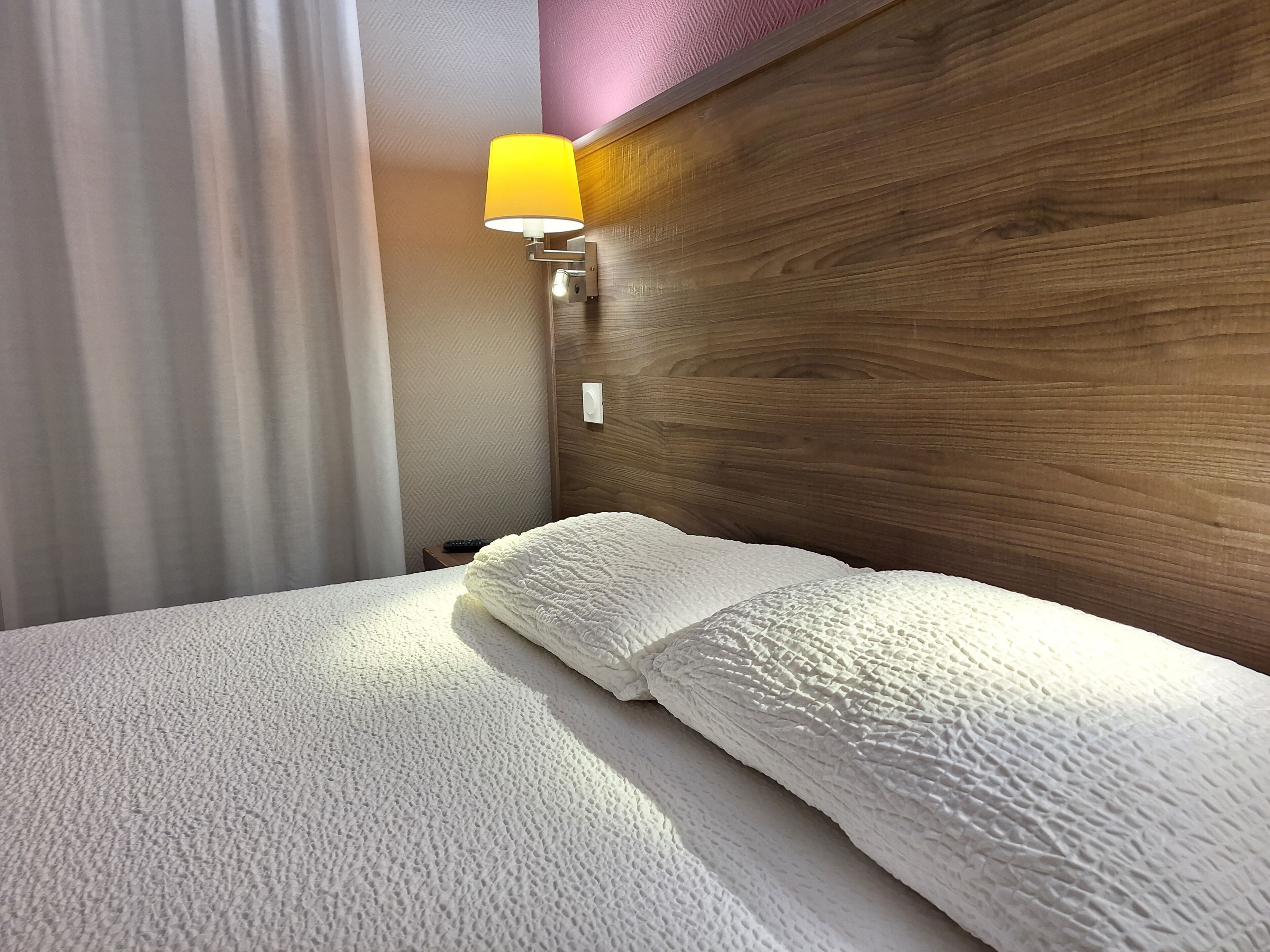 A hotel room with a bed, a nightstand, a lamp, and a wooden headboard.