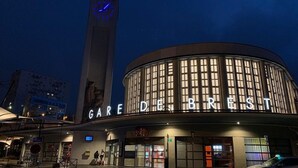 Un edificio con una destacada torre de reloj y el nombre 'GARE DE BREST' iluminado en la fachada.