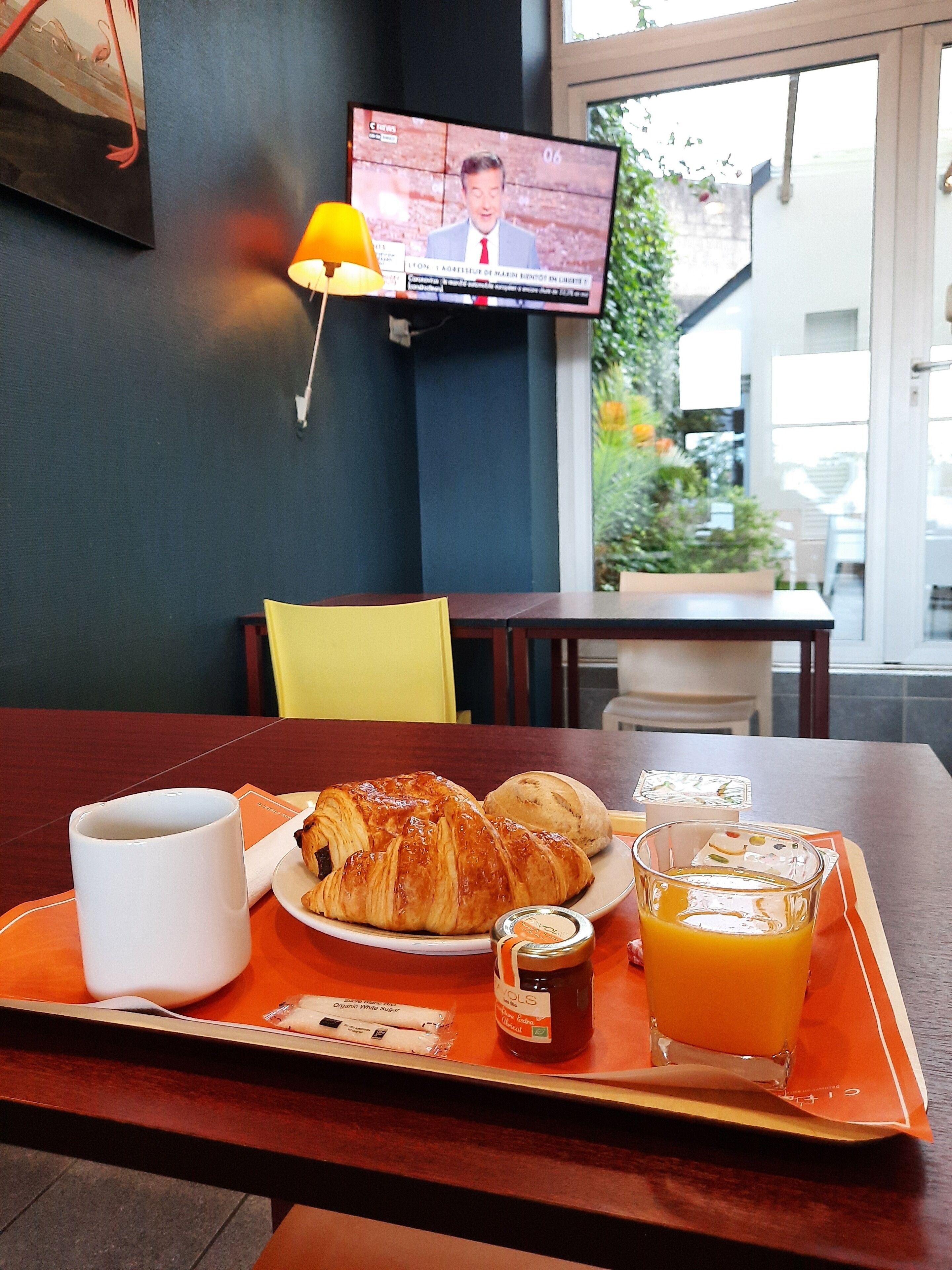 Ein Frühstücksbrett mit Croissants, einem Glas Orangensaft und einer kleinen Marmeladendose auf einem Tisch in einem Café.