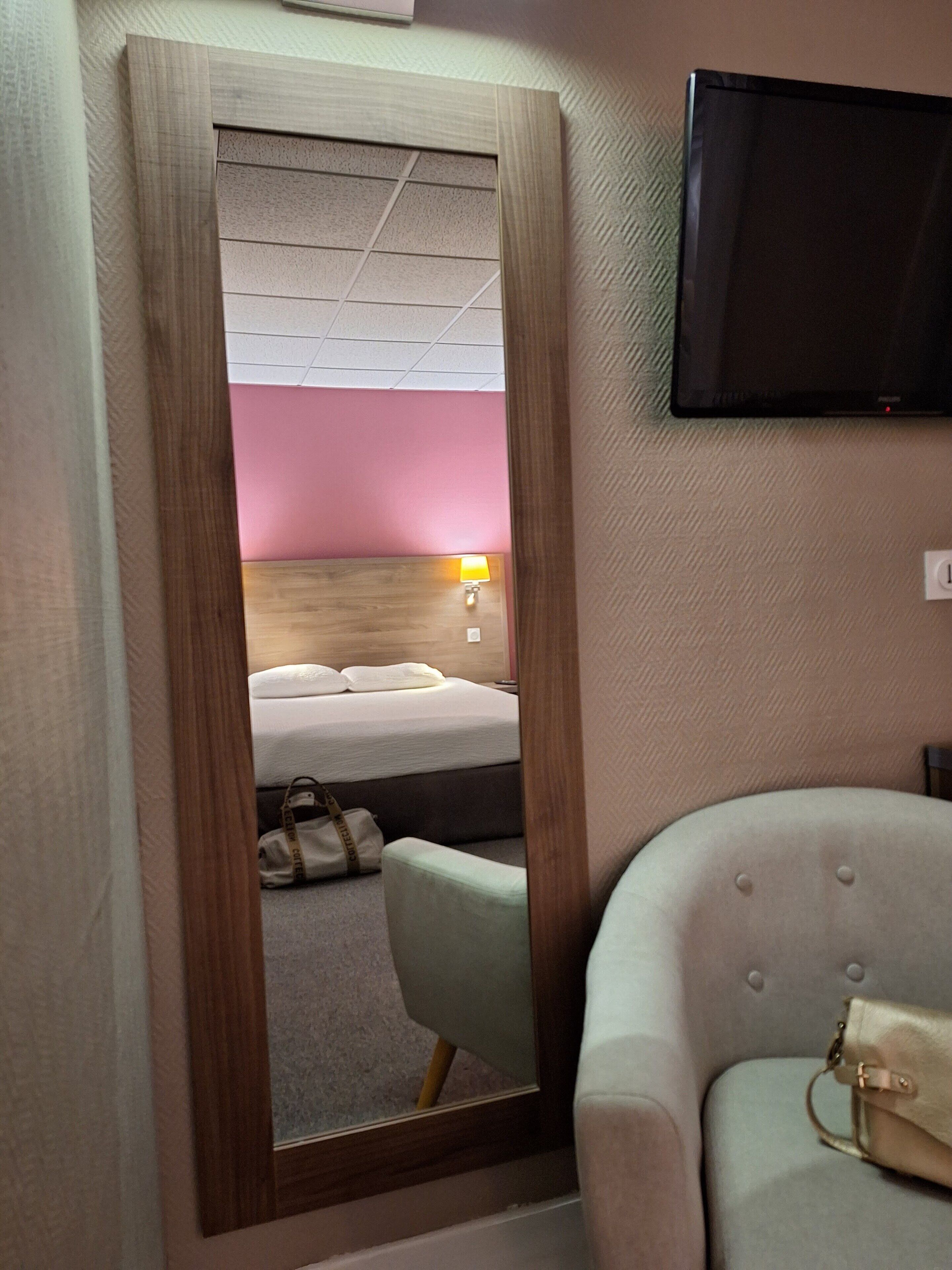 A hotel room with a bed, a chair, a bedside table, a lamp, and a TV mounted on the wall.