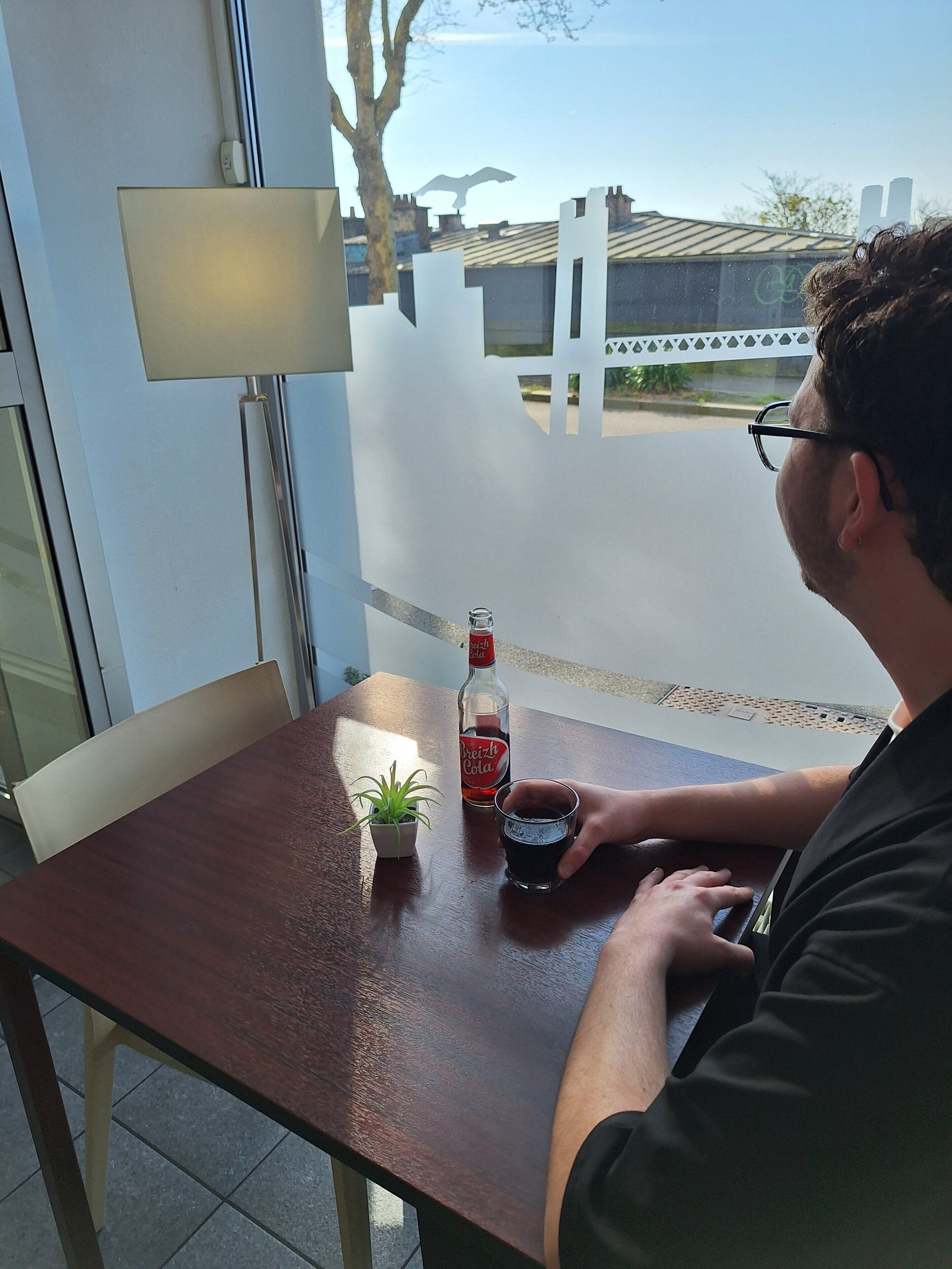 A man sitting at a table with a bottle of beer, a glass, and a small plant.