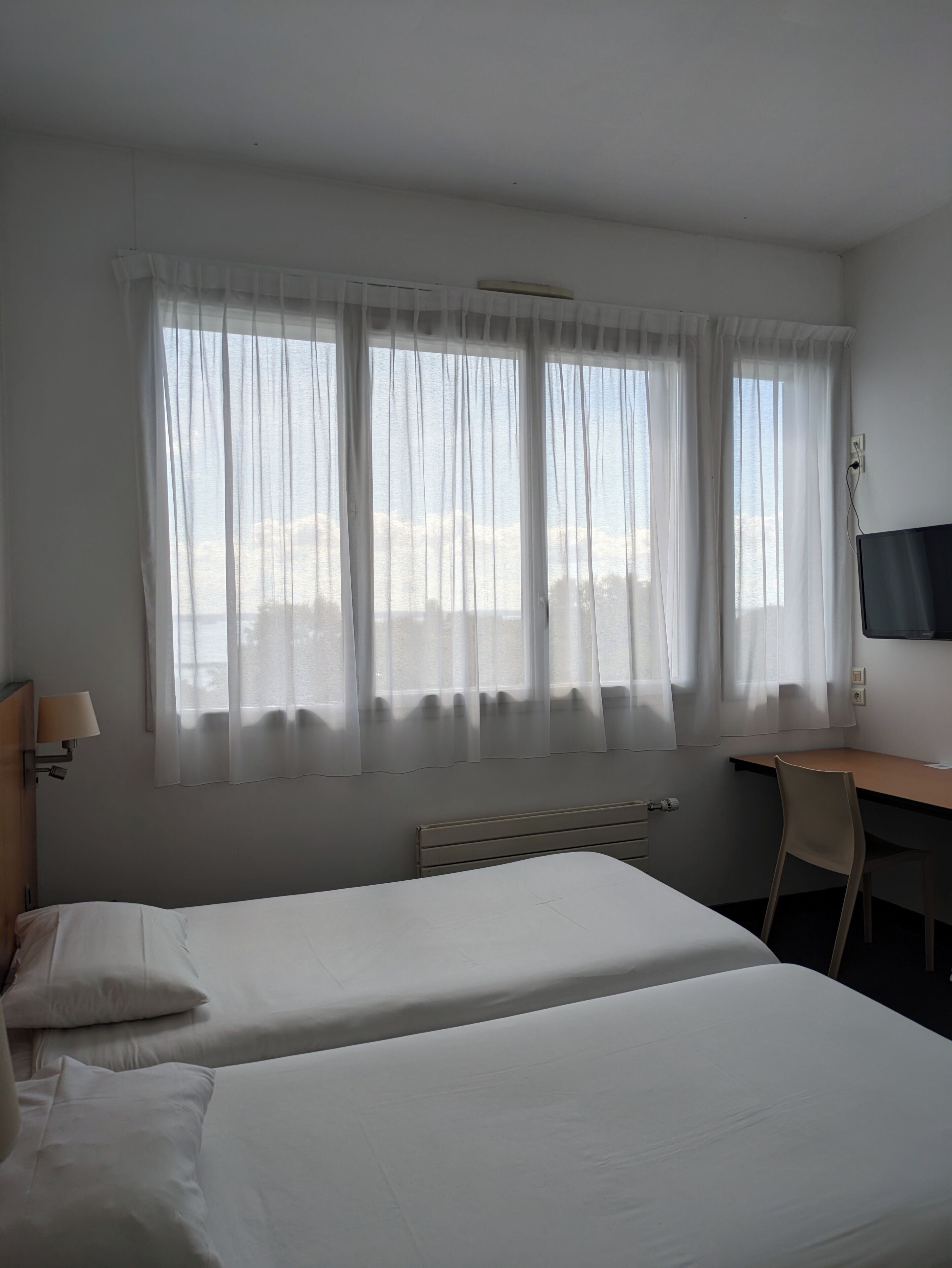 A hotel room with two beds, a desk, a chair, and a TV.