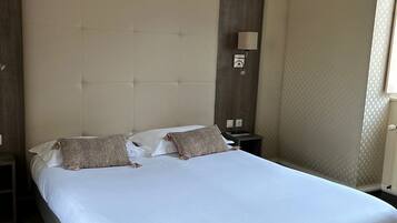 A neatly made bed in a hotel room with a headboard, a bedside table, and a lamp.