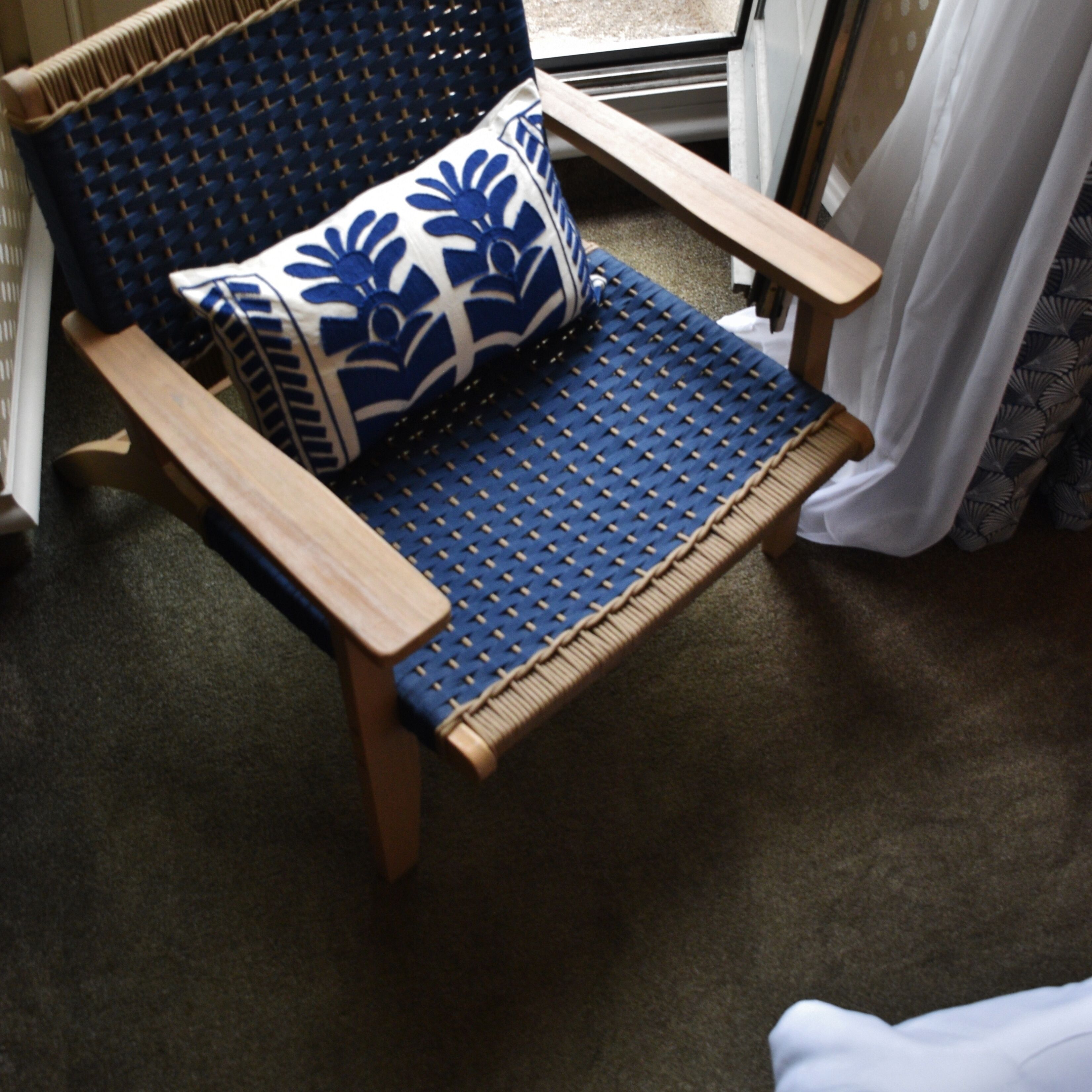 A chair with a woven seat and backrest, a blue and white patterned pillow, and wooden armrests.