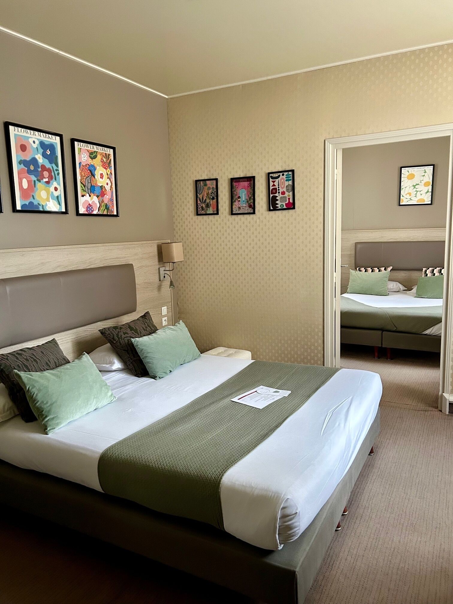 Een hotelkamer met een groot bed, een nachtkastje, een wandlamp en drie ingelijste kunstwerken boven het bed.