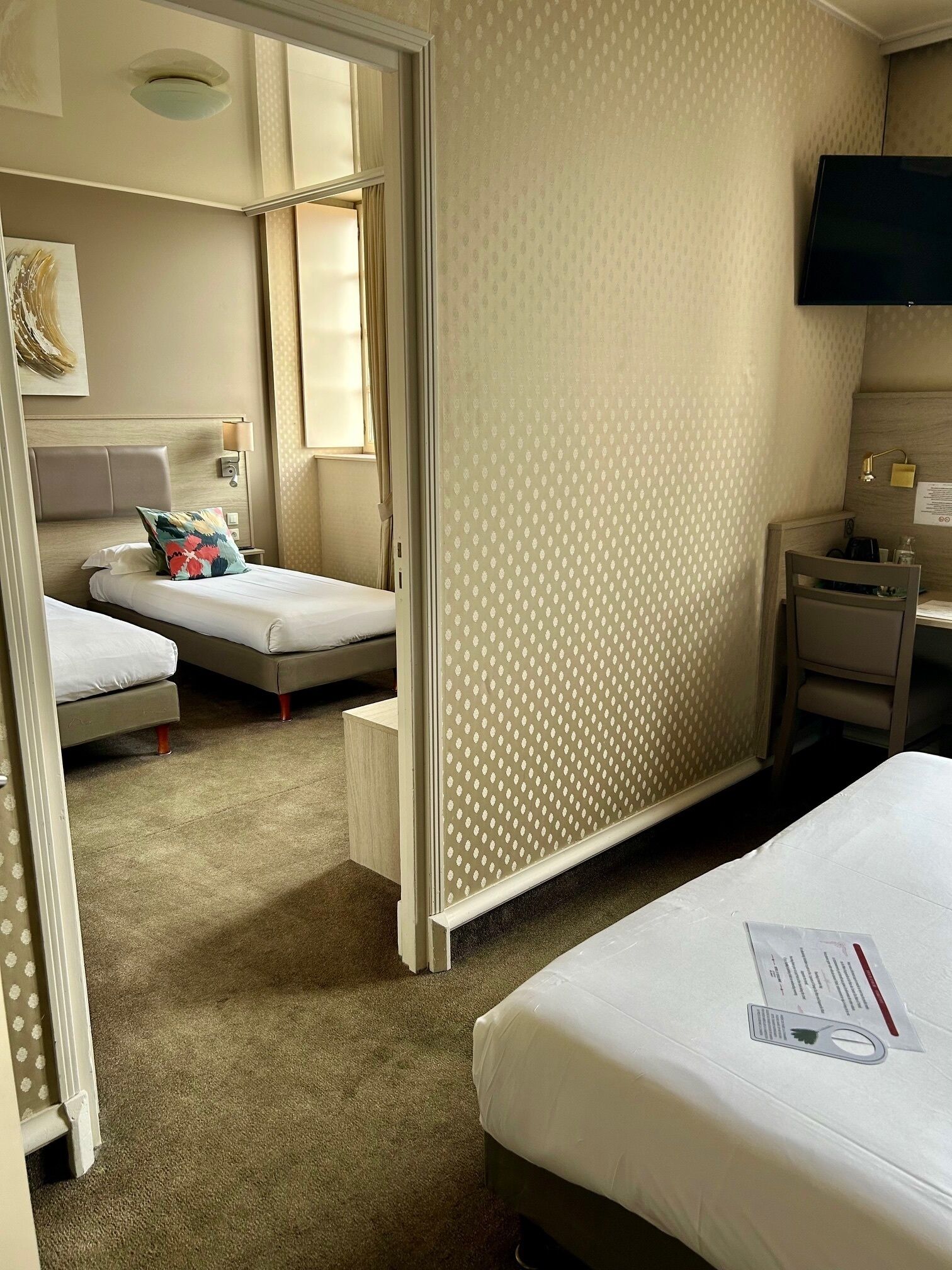 Habitación de hotel con dos camas individuales, un escritorio con silla, televisor y pared con diseño.