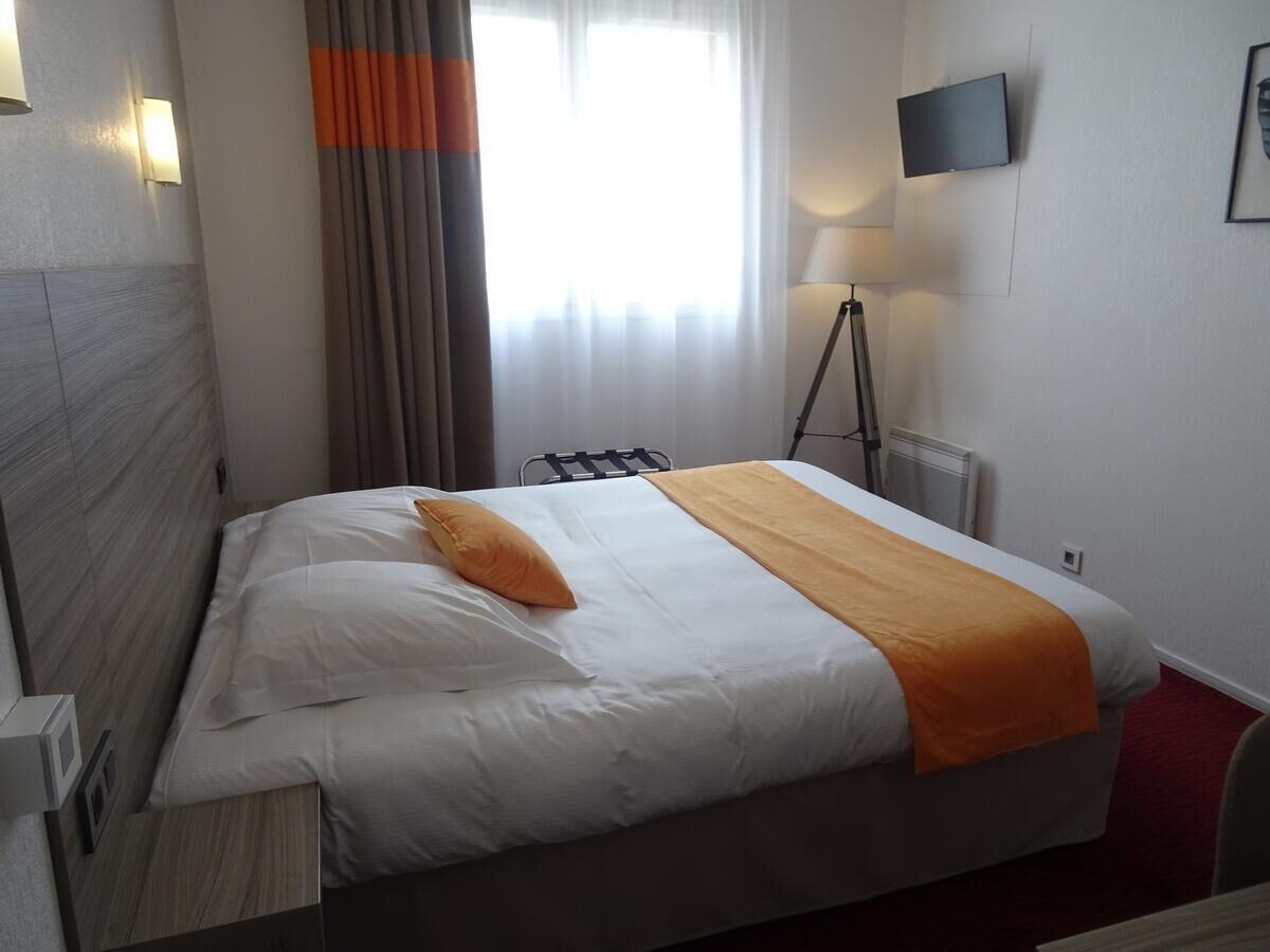 A hotel room with a bed, a lamp, a TV, and a window with curtains.