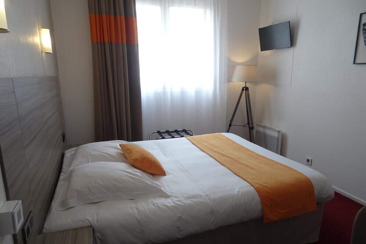 A hotel room with a bed, a lamp, a TV, and a window with curtains.