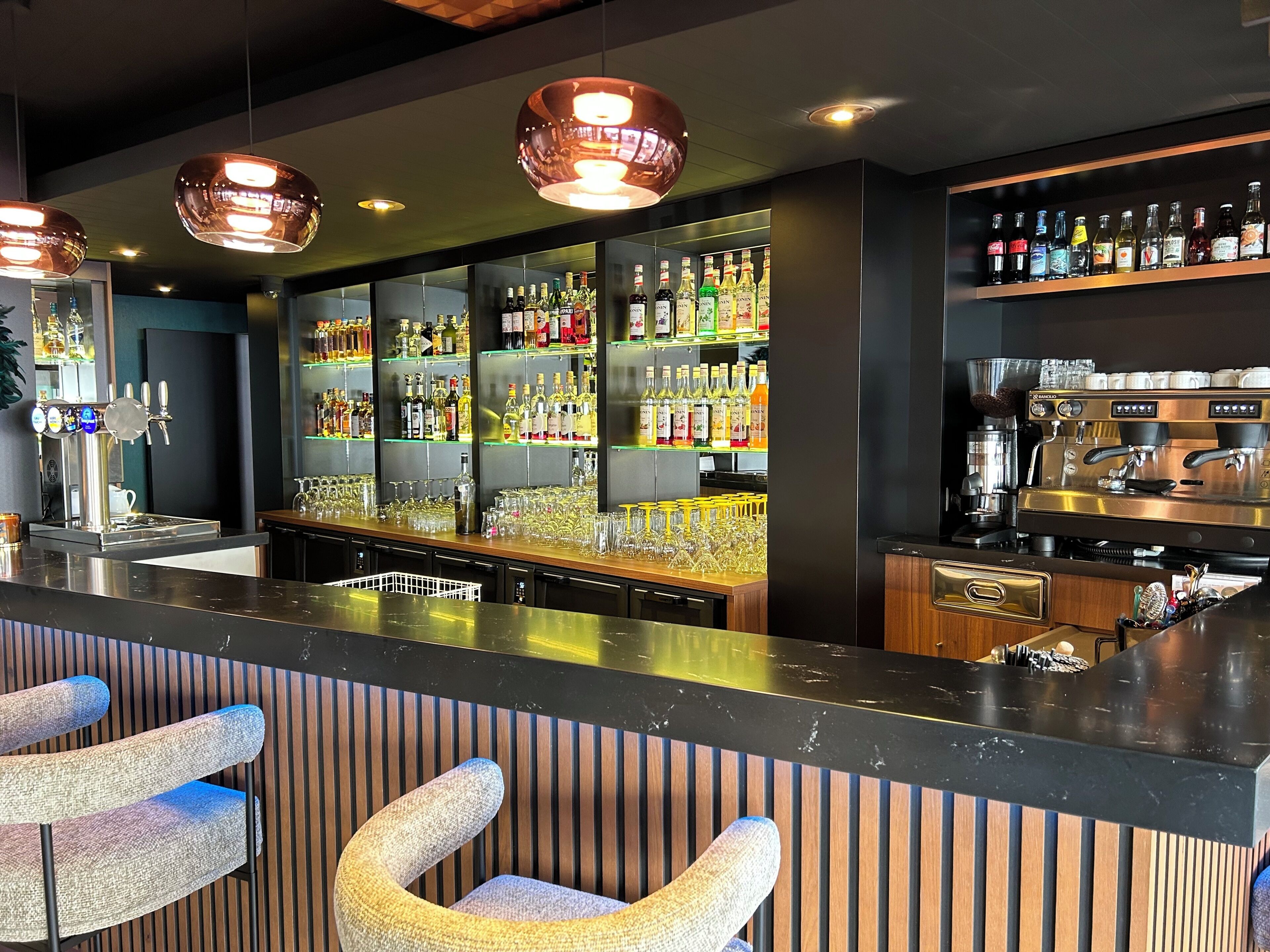 Zona de bar con mostrador, asientos y una variedad de botellas y vasos.
