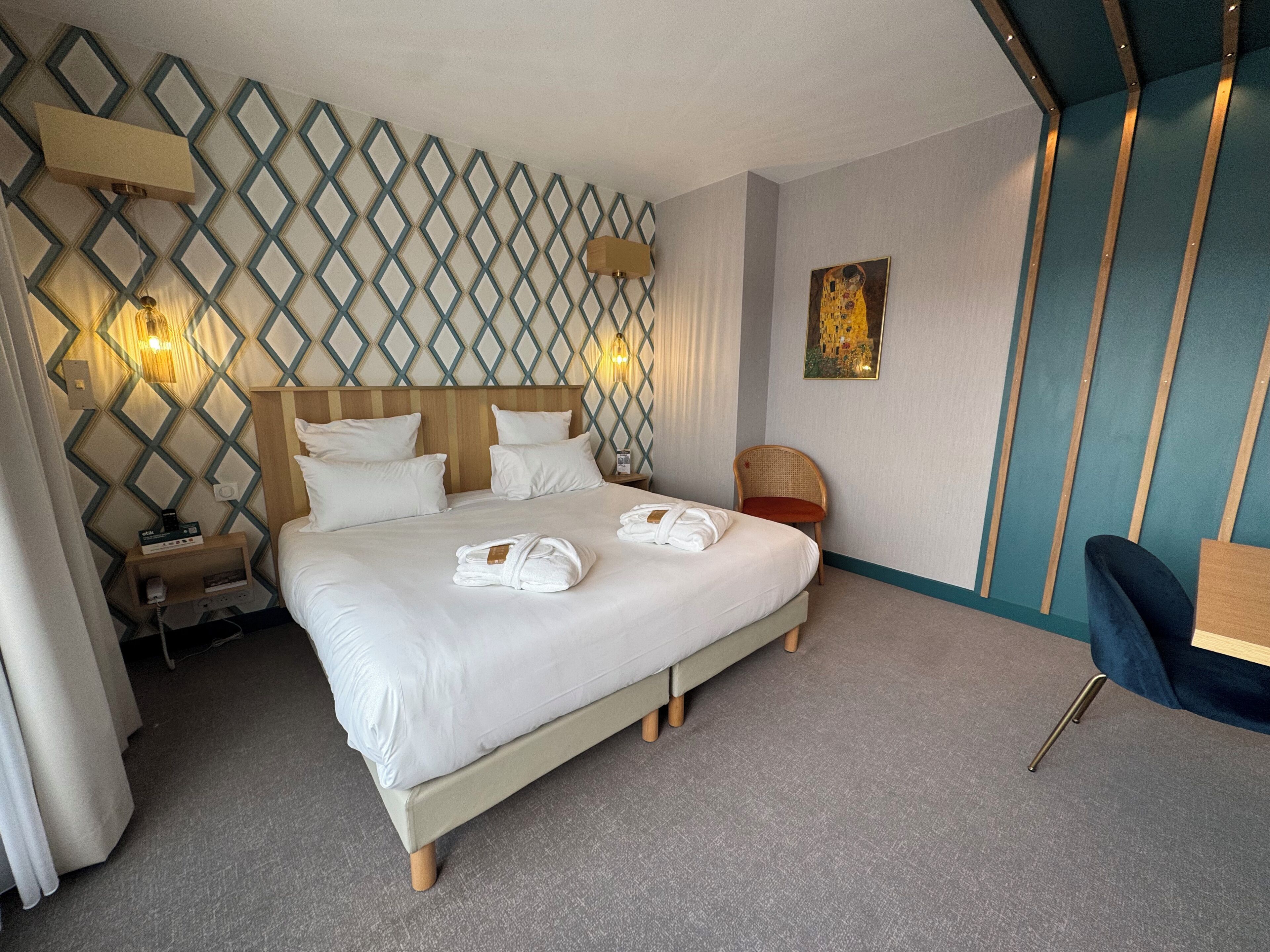 Habitación de hotel con una cama grande, cabecero de madera, lámpara de pared, un cuadro y una silla.