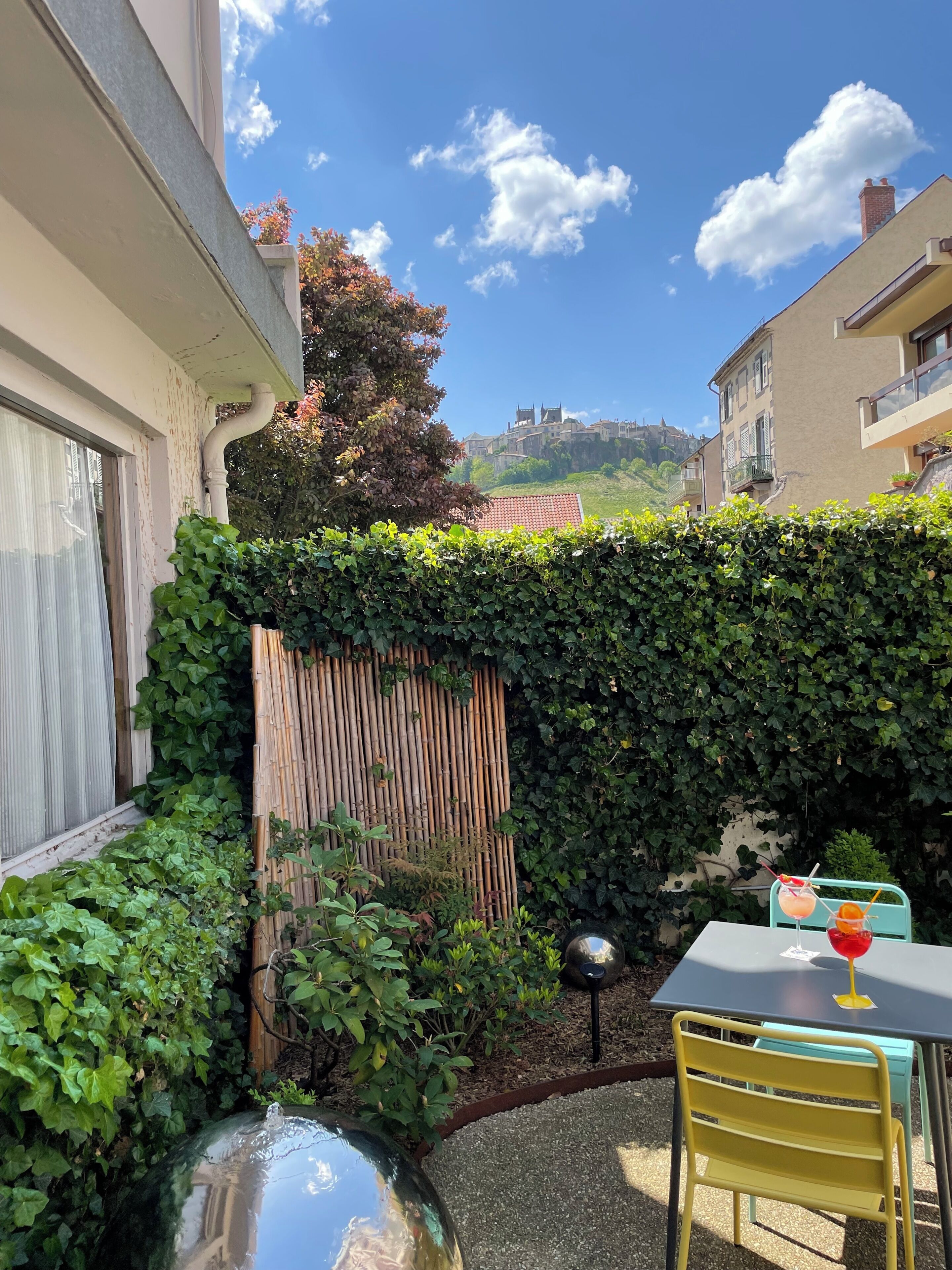 A courtyard with a table and chairs, a bamboo fence, and a view of buildings in the distance.