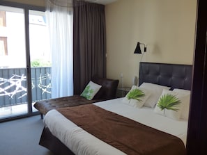 A hotel room with a large bed, a chair, a desk, and a balcony with a view.