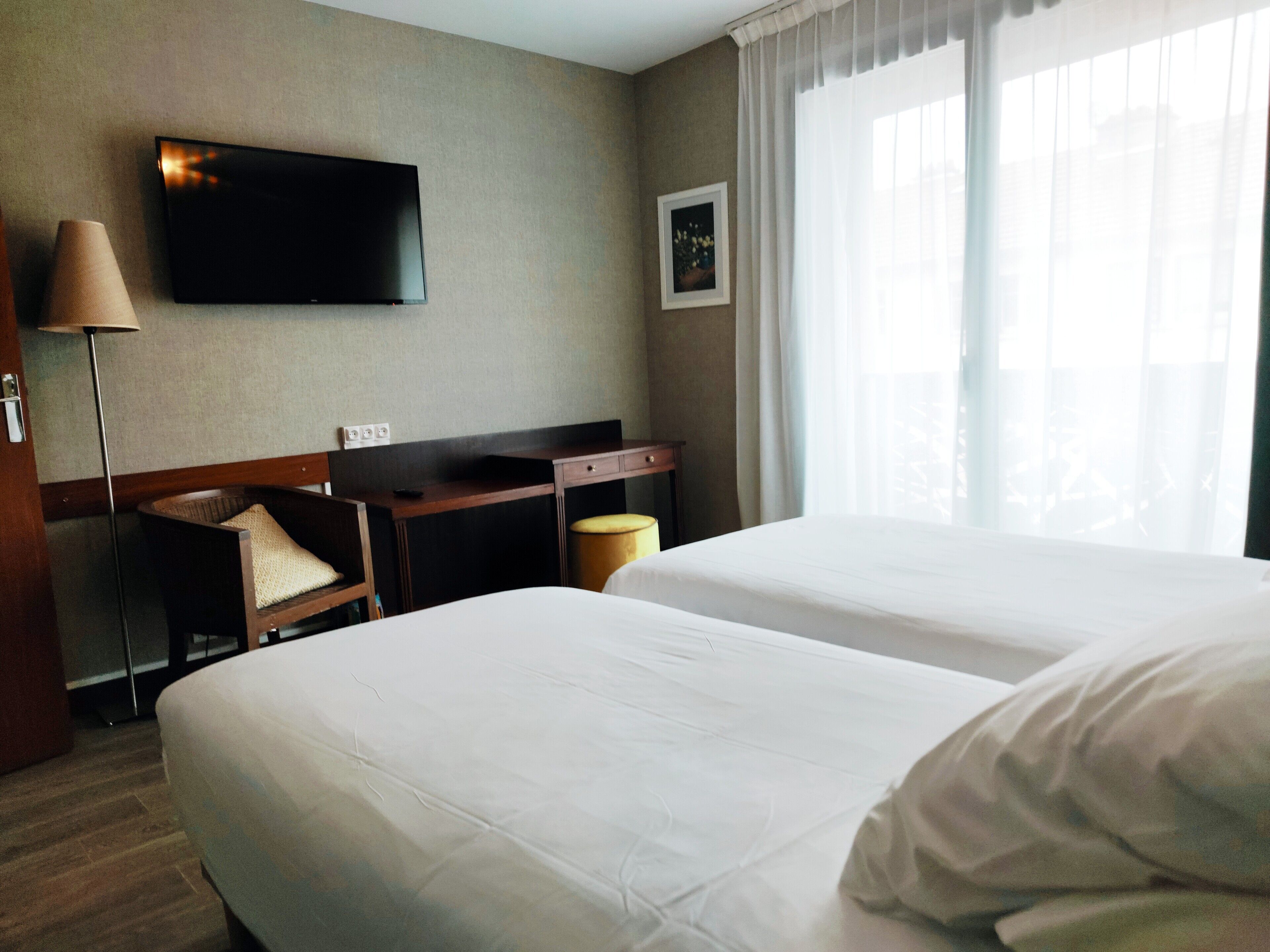 A hotel room with two beds, a desk, a chair, a TV, and a window with curtains.
