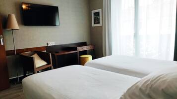 A hotel room with two beds, a desk, a chair, a TV, and a window with curtains.