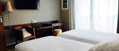 Habitación de hotel con dos camas, un escritorio, una silla, un televisor y una ventana con cortinas.