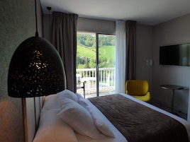 Habitación de hotel con cama, televisor, balcón con vistas a la vegetación y una silla amarilla.