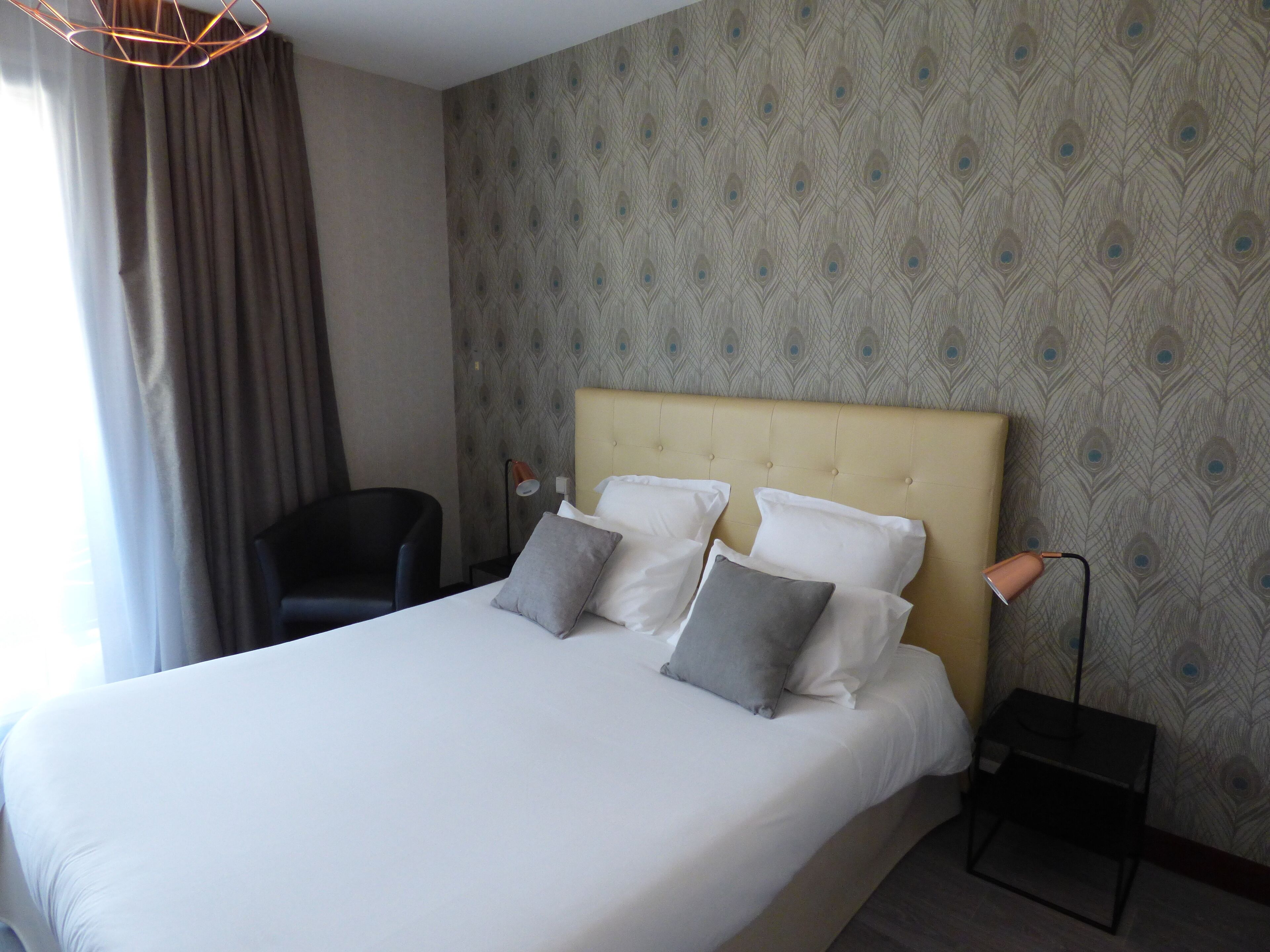 Una habitación de hotel con una cama grande, una silla, una mesita de noche y una lámpara.