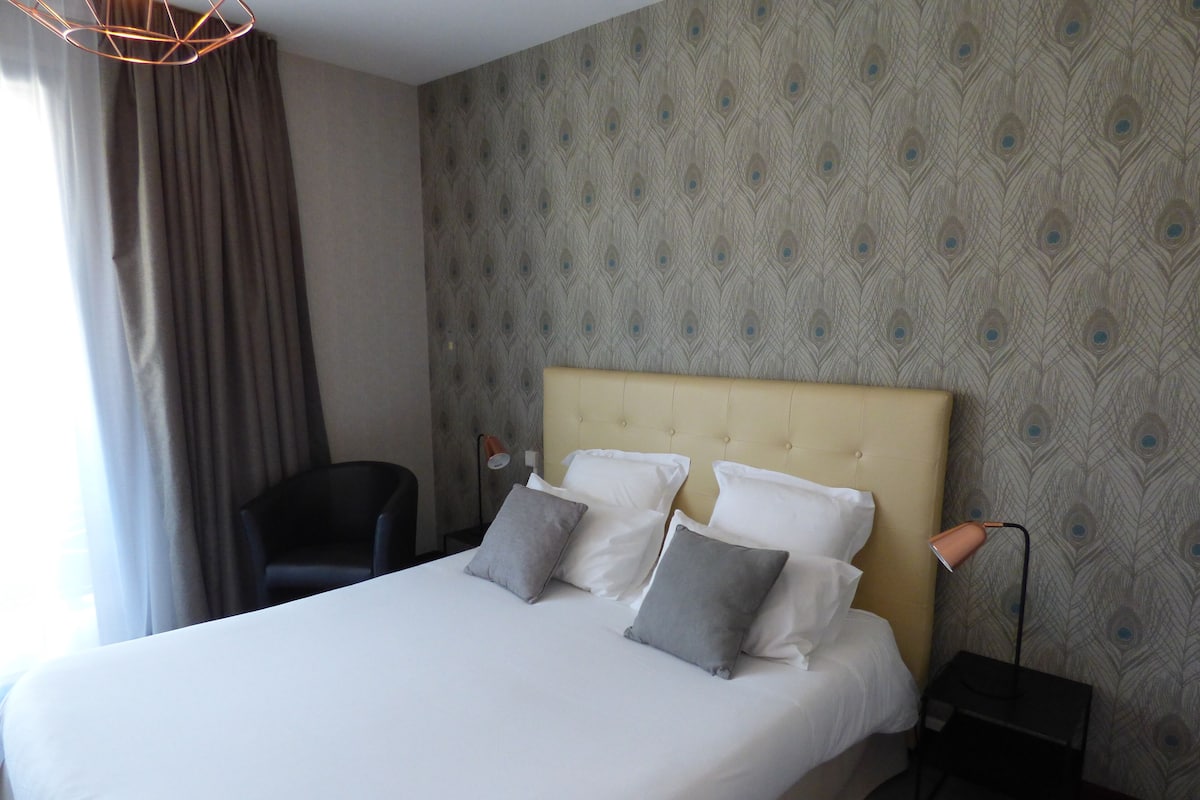 A hotel room with a large bed, a chair, a bedside table, and a lamp.