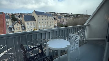 Un balcon avec une table et deux chaises, donnant sur un quartier résidentiel avec des immeubles et un ciel dégagé.