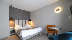 A modern hotel room with a bed, bedside lamps, a small table, and a chair.