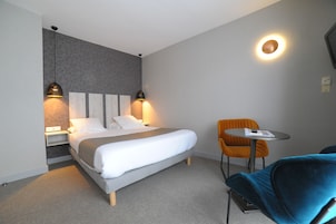 Una habitación de hotel moderna con cama, lámparas de noche, una mesita y una silla.