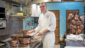 A chef in a professional kitchen with stainless steel appliances, copper pots, and a variety of cooking utensils.