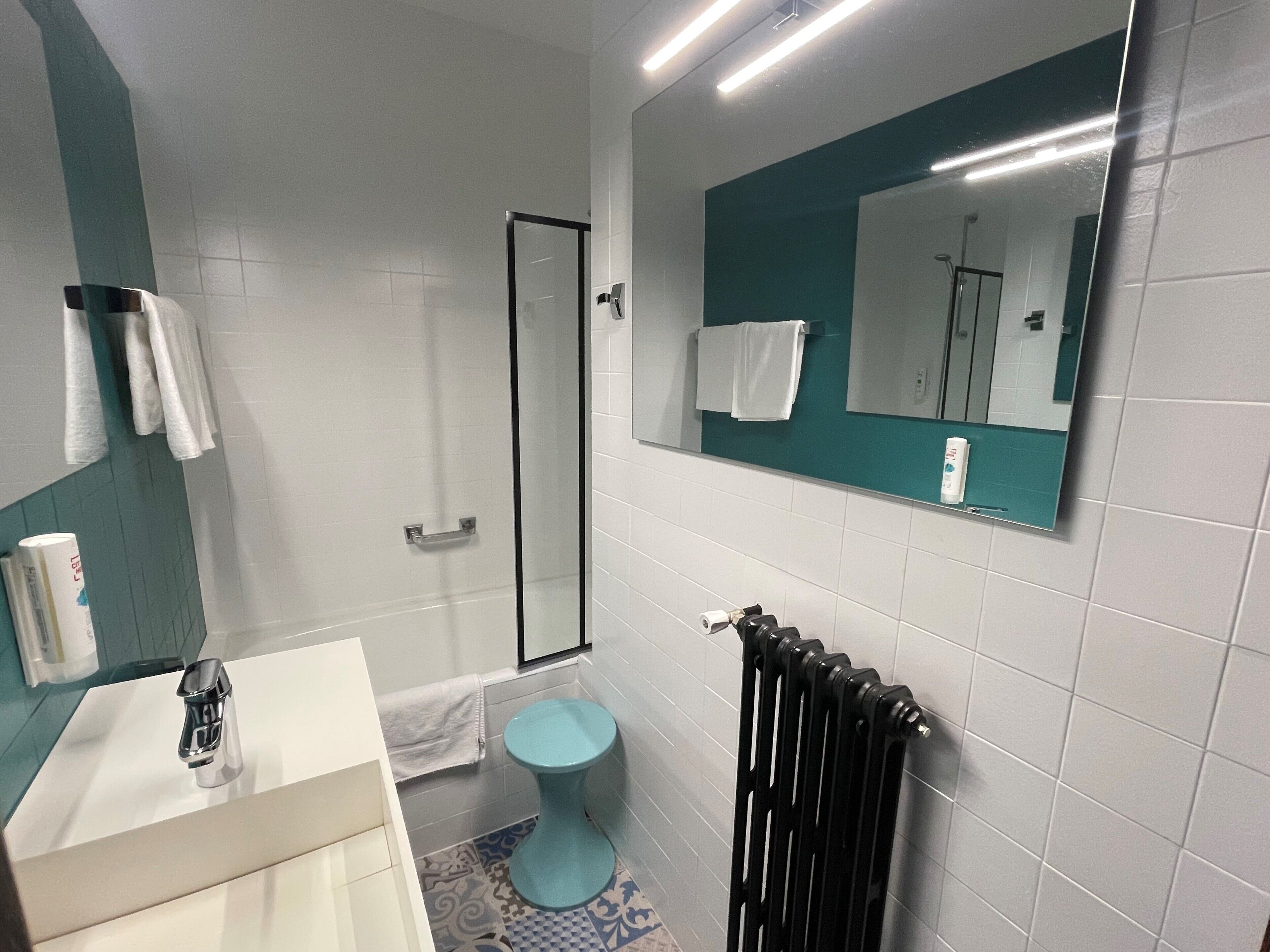 A bathroom with a white sink, a blue toilet, a glass shower enclosure, and a mirror with a teal frame.