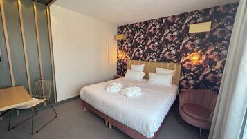 Une chambre d’hôtel avec un lit, une chaise, une table et un papier peint à motifs floraux.